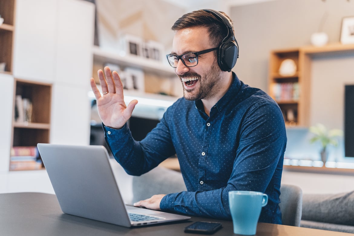 Man at laptop working from home, waving hello to colleagues